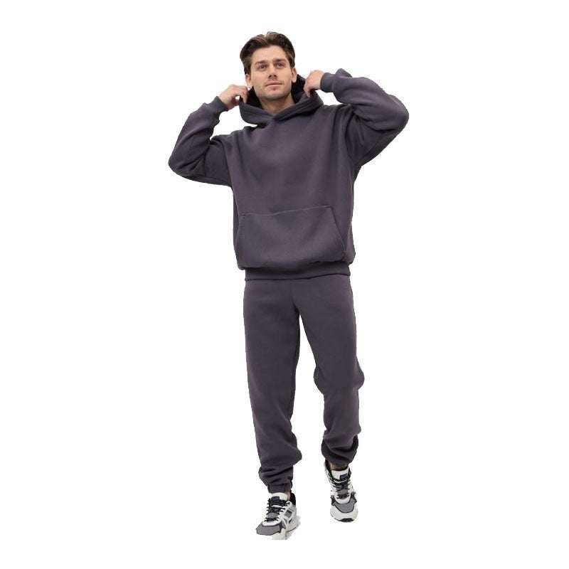 Man wearing dark gray hoodie two-piece set with matching joggers and sneakers standing isolated on white background