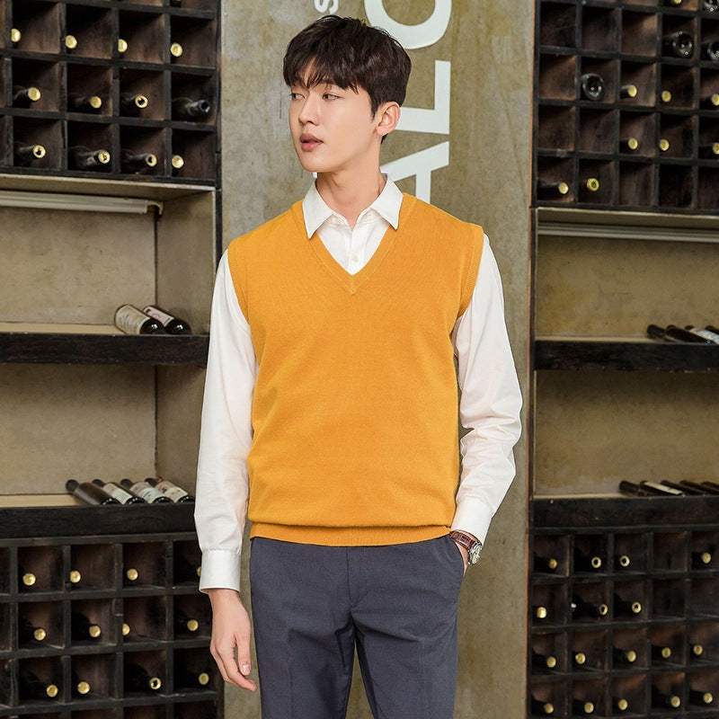 Man wearing mustard yellow mens vest pullover over white shirt with dark trousers in casual indoor setting