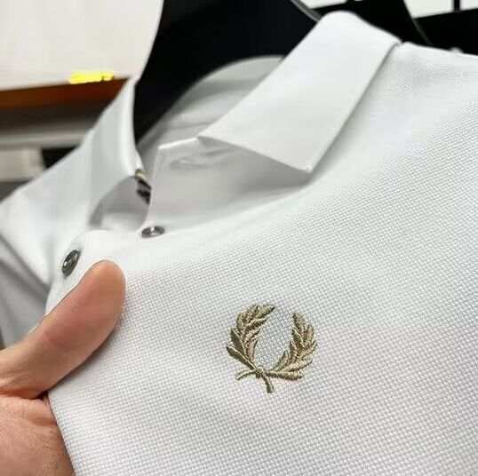 Close-up of men's lapel half sleeve white polo shirt with embroidered logo and button details.