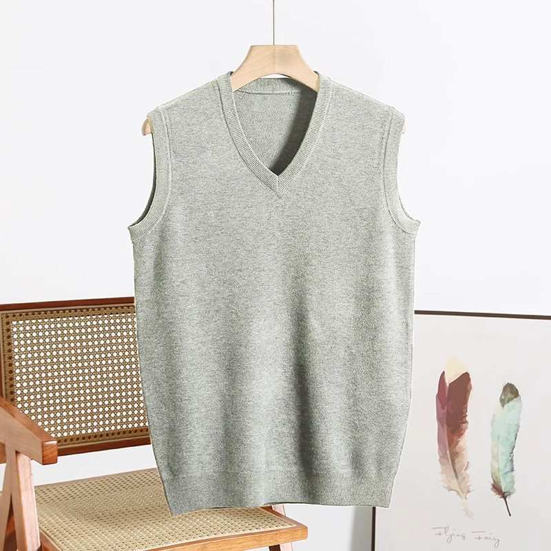 Men's grey V-neck sweater vest hanging on wooden hanger, displayed with chair and feather artwork.