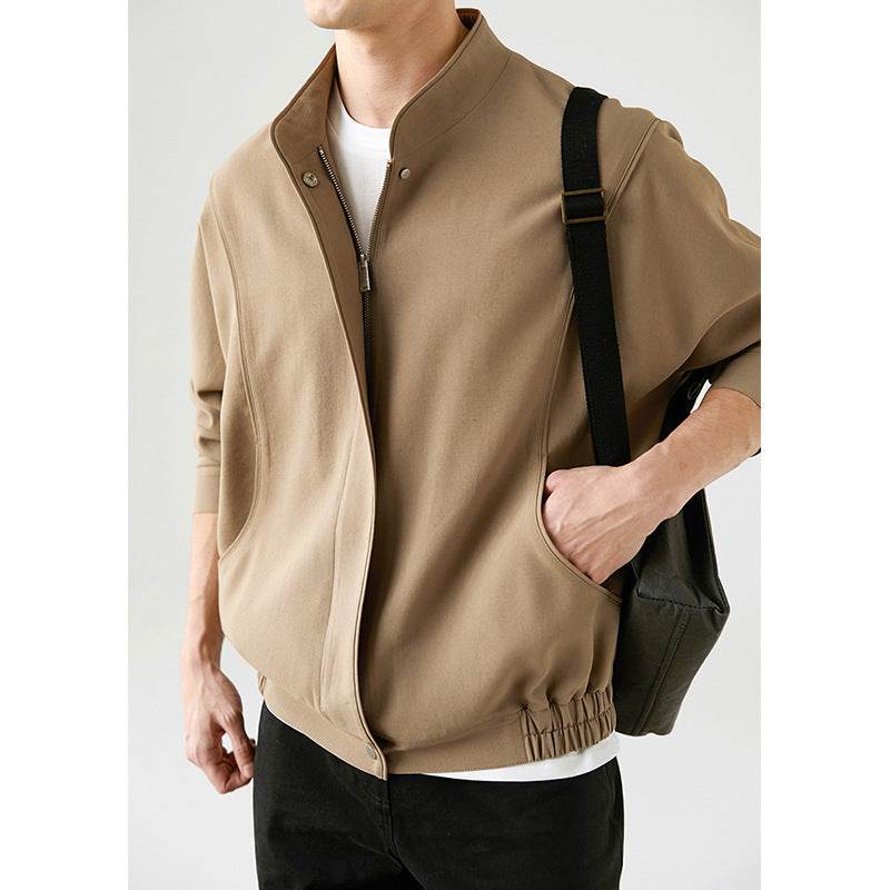 Loose casual pilot jacket in khaki polyester with elastic hem and zipper closure, worn by a young man carrying a black shoulder bag.